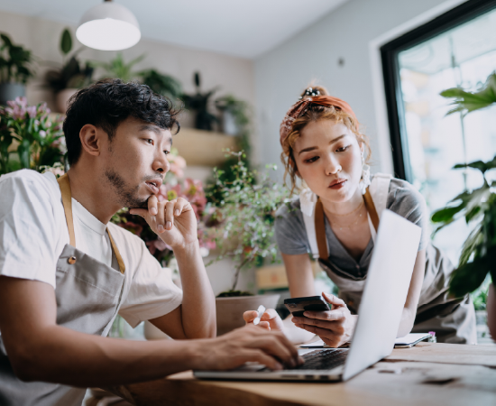 Two small business owners planning together on a laptop in a plant-filled workspace