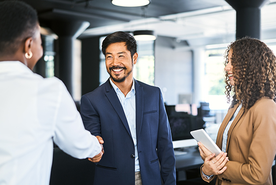 Asian man shaking hand with black woman and a second woman standing nearby