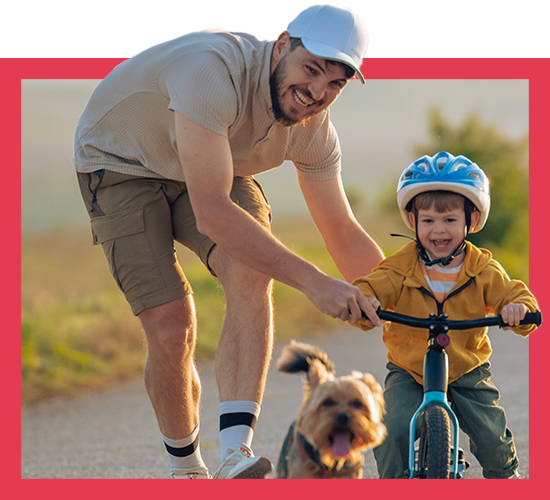 Father teaching song to ride a bike with dog running beside them