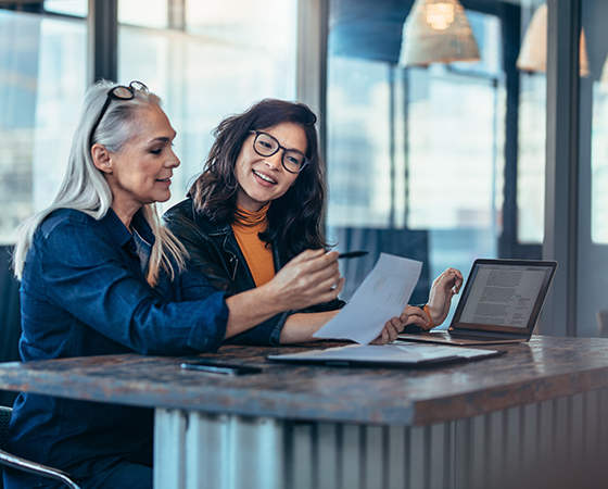 Two women reviewing paperwork in front of a laptop.