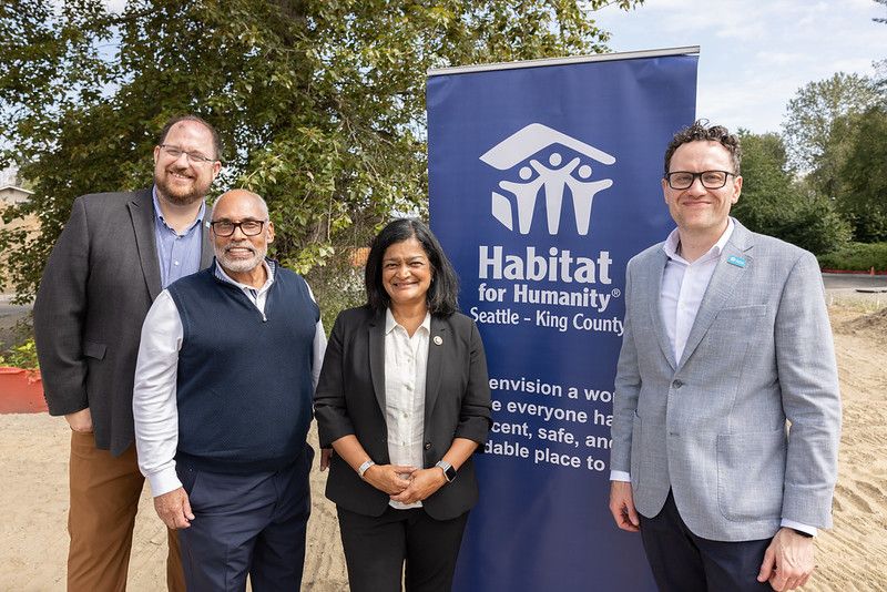 Group of representatives standing in front of a sign at a groundbreaking ceremony.