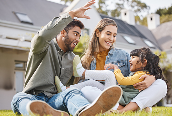 Hispanic dad, mom and young daughter on the grass in front of a house