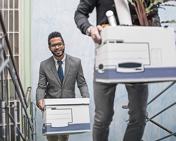 2 men walking up stairs in an office carrying offices boxes.