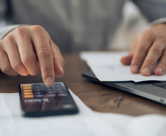 Hands using a calculator and reviewing documents on a table.