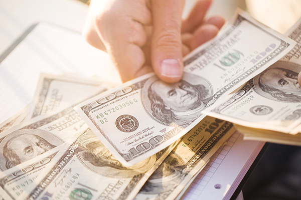 hand holding $100 bill with other $100 bills in the background