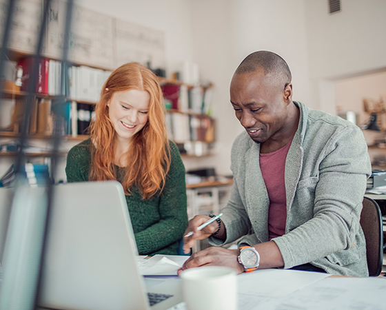 Man and woman reviewing paperwork in front of a laptop inside a small office.